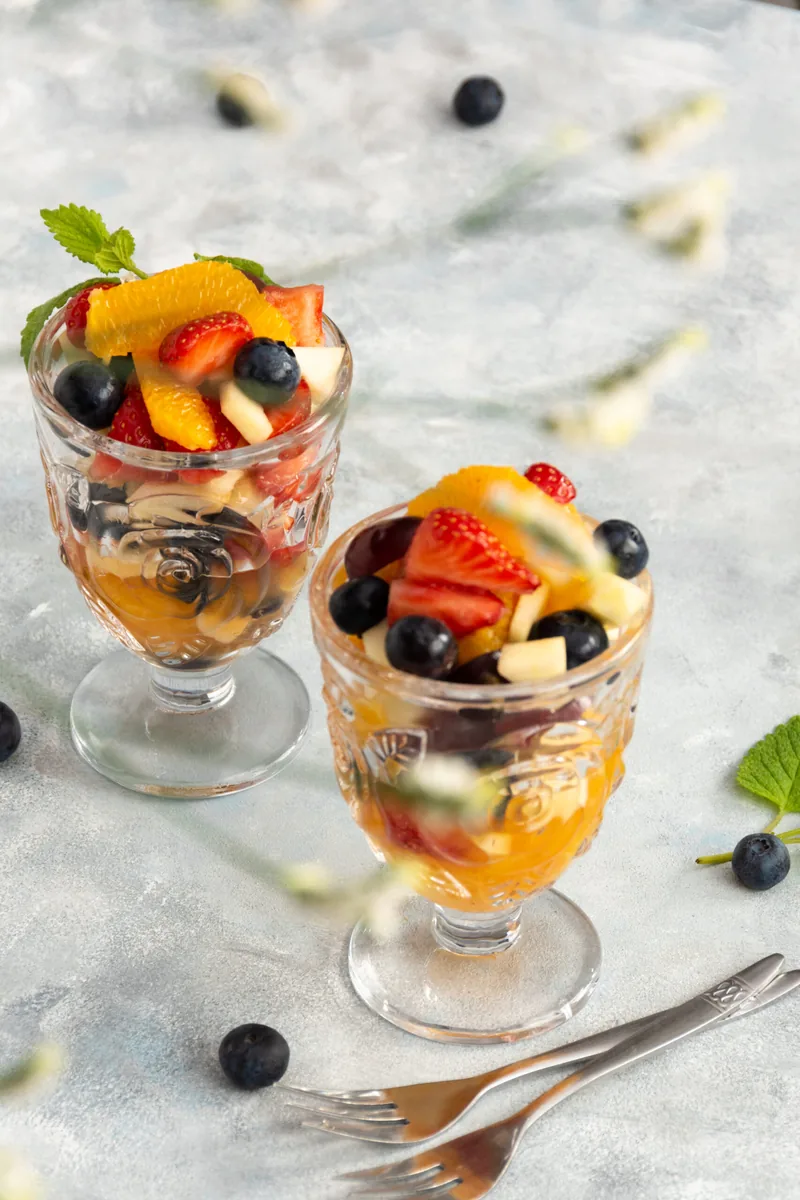 Twee glazen coupes met vers fruit: sinaasappel, aardbei en blauwe bessen