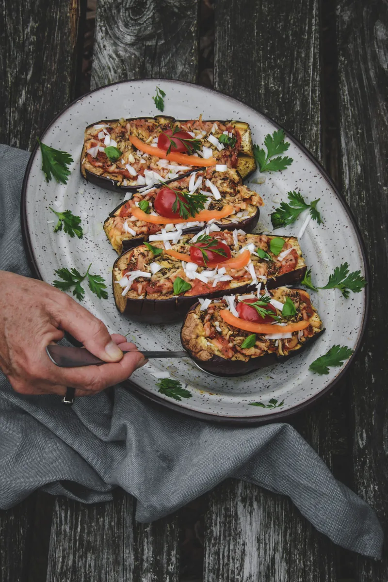 Gevulde halve aubergines met tomaat, wortel en peterselie op een grijze schaal, op een donkere houten tafel