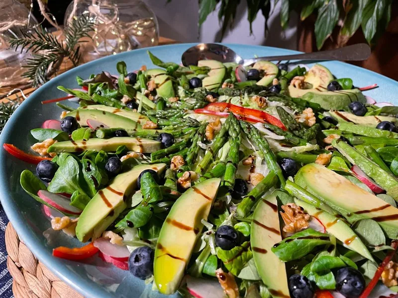 Een grote blauwe schaal met salade: veldsla, avocado, groene asperges, blauwe bessen en walnoten